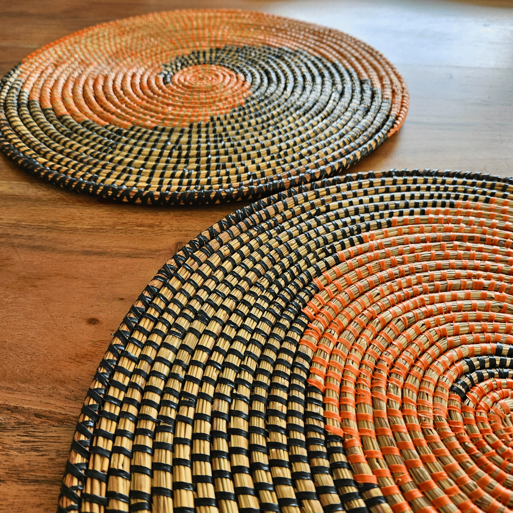 Image d'un duo de sets de table oranges et noirs tressés ronds en fibres naturelles